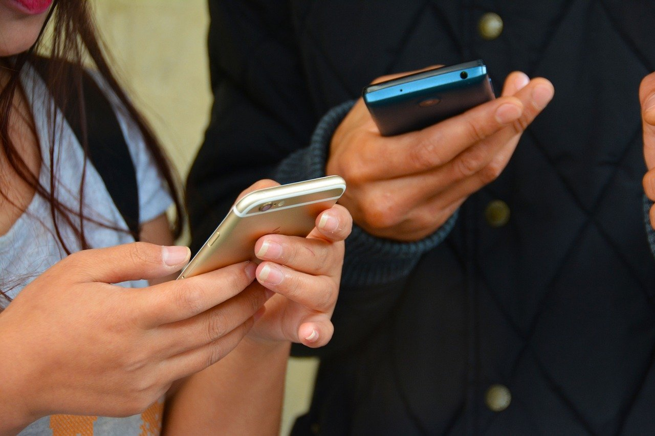 Close-up of man and woman standing next to each other holding cell phones