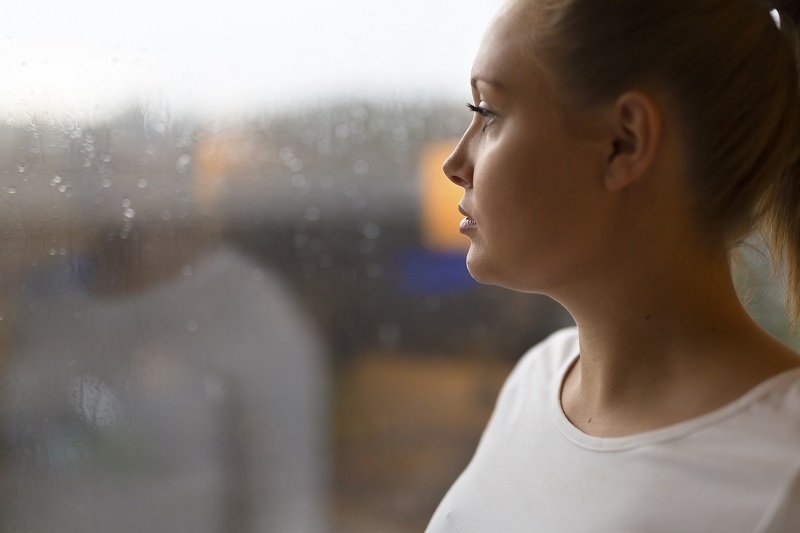 Young woman with thoughtful expression looking out the window.