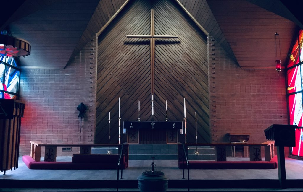 dimly lit interior of a brown brick church with wooden cross at front