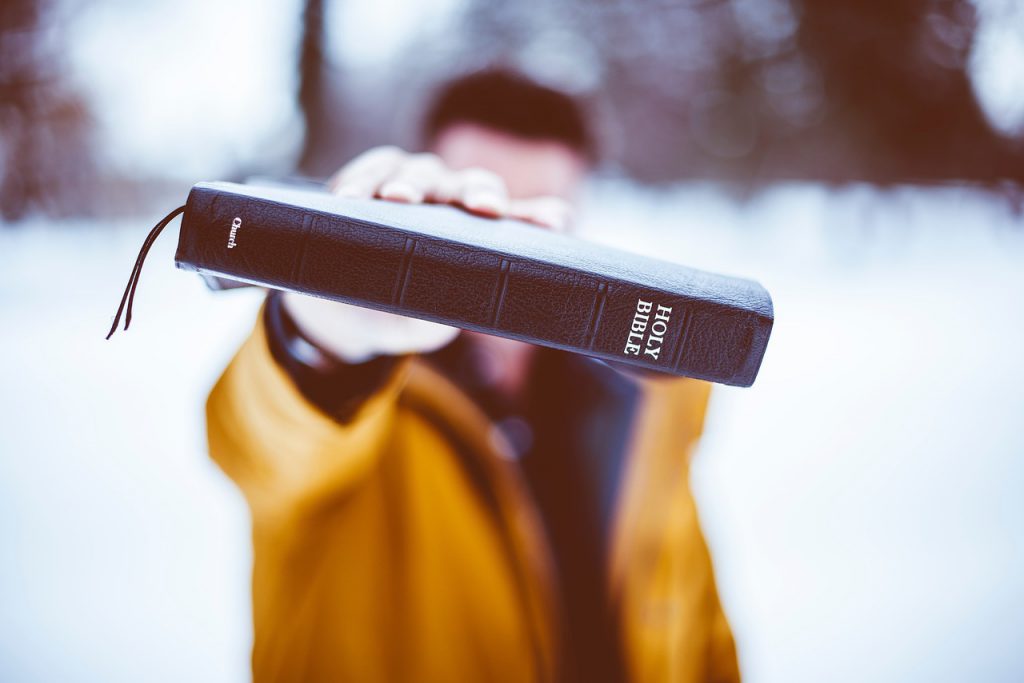 Close up shot of a Holy Bible spine, held up by a man wearing a yellow jacket blurred in the background